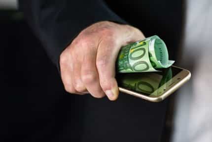 Mann hält einen 100-Euro-Schein und ein Smartphone in seiner Hand